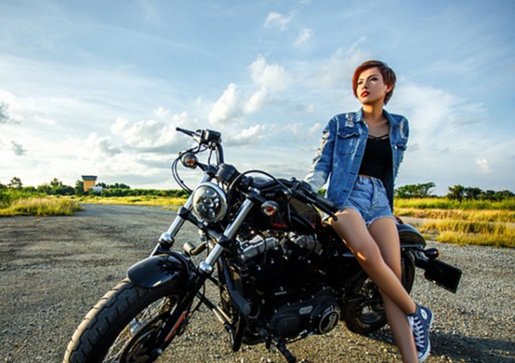 Kobieta opierająca się o motocykl Rękawice motocyklowe damskie - jakie kupić